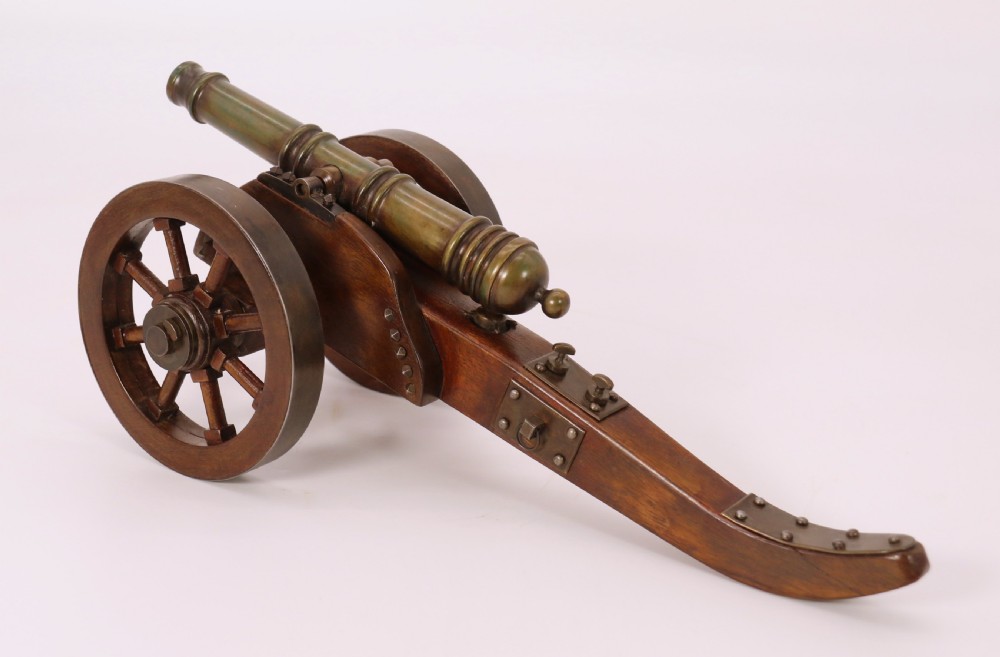 A detailed hand-built scale model of a 17th-century field cannon featuring a patinated brass barrel mounted on a dark timber carriage with spoked wheels. View VI