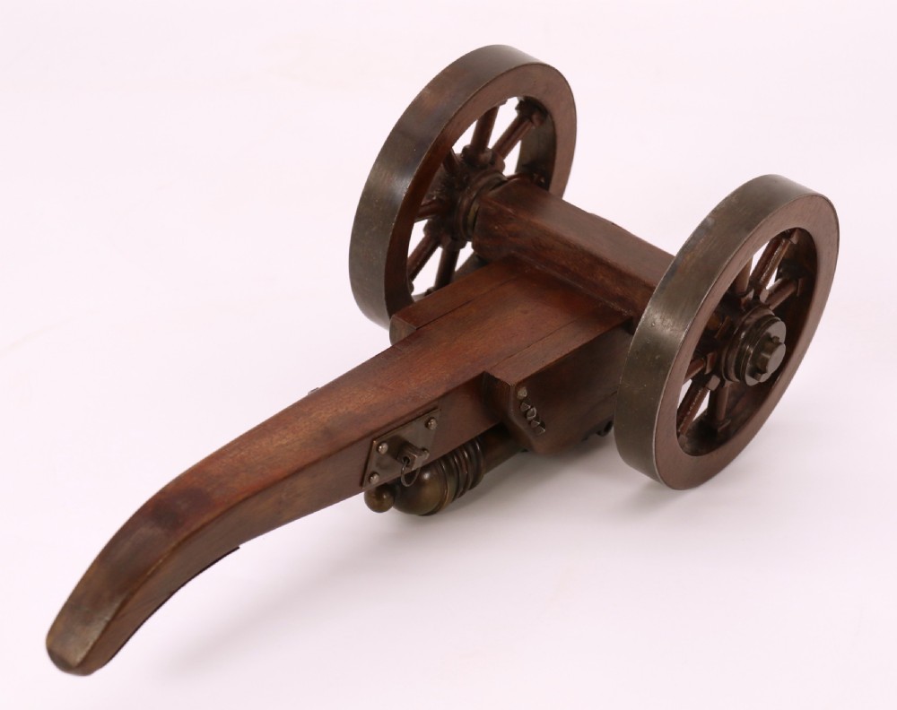 A detailed hand-built scale model of a 17th-century field cannon featuring a patinated brass barrel mounted on a dark timber carriage with spoked wheels. View X
