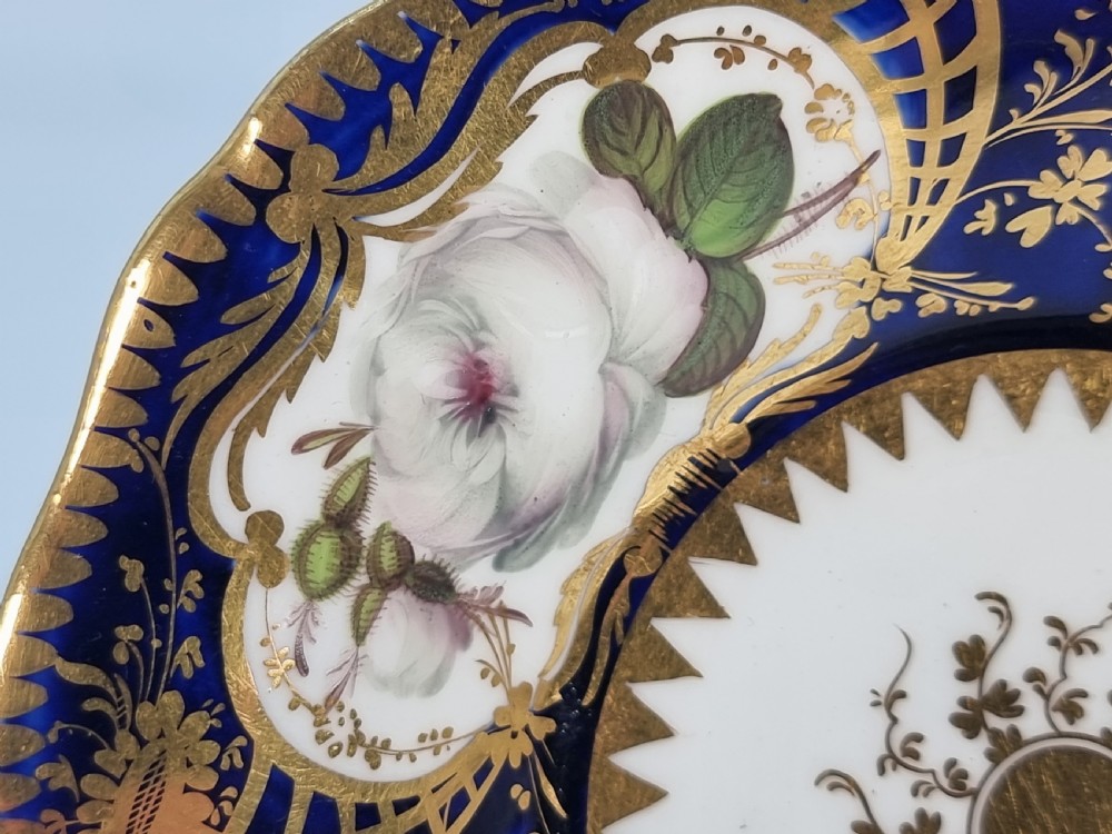 An early nineteenth-century Coalport porcelain cabinet trio featuring a teacup, coffee cup, and saucer styled with cobalt blue borders, gilded detailing, and hand-painted white rose panels. View II