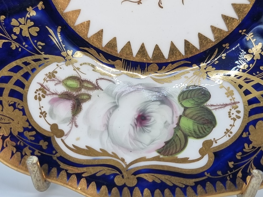 An early nineteenth-century Coalport porcelain cabinet trio featuring a teacup, coffee cup, and saucer styled with cobalt blue borders, gilded detailing, and hand-painted white rose panels. View VI