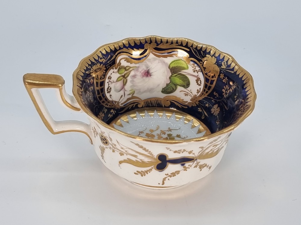 An early nineteenth-century Coalport porcelain cabinet trio featuring a teacup, coffee cup, and saucer styled with cobalt blue borders, gilded detailing, and hand-painted white rose panels. View VII