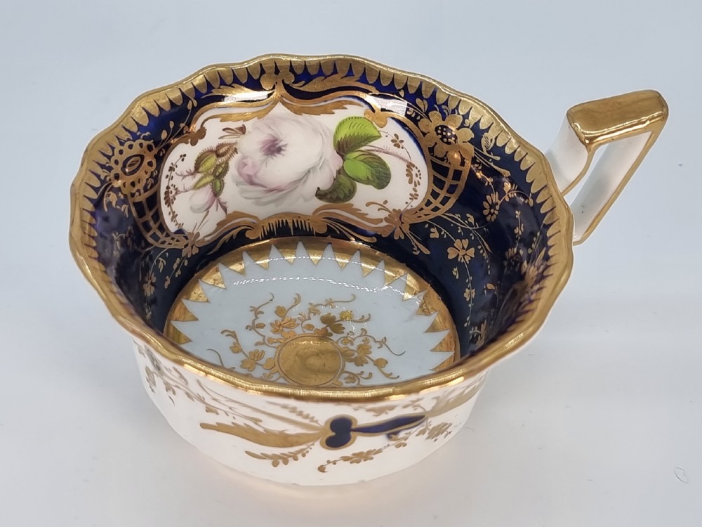An early nineteenth-century Coalport porcelain cabinet trio featuring a teacup, coffee cup, and saucer styled with cobalt blue borders, gilded detailing, and hand-painted white rose panels. View VIII