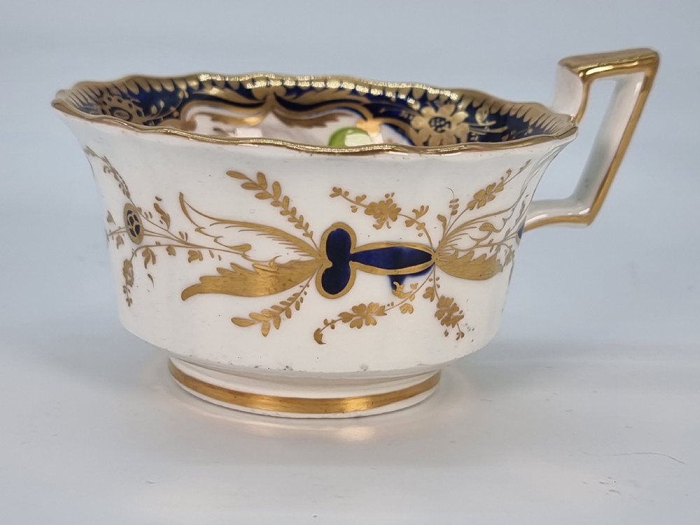An early nineteenth-century Coalport porcelain cabinet trio featuring a teacup, coffee cup, and saucer styled with cobalt blue borders, gilded detailing, and hand-painted white rose panels. View IX