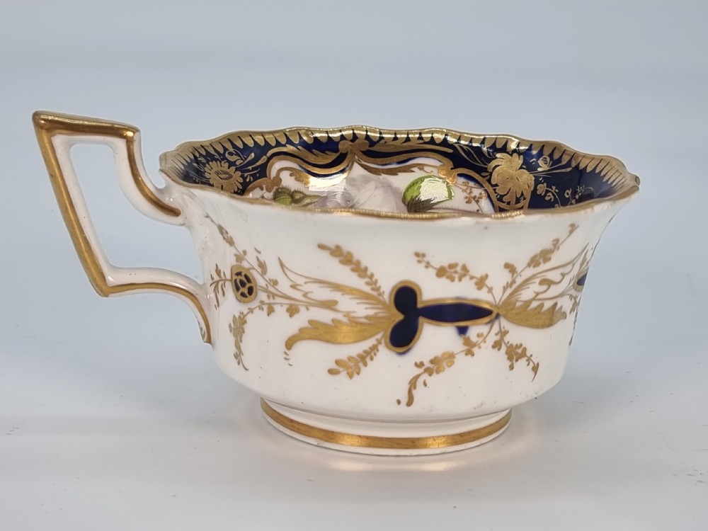 An early nineteenth-century Coalport porcelain cabinet trio featuring a teacup, coffee cup, and saucer styled with cobalt blue borders, gilded detailing, and hand-painted white rose panels. View X