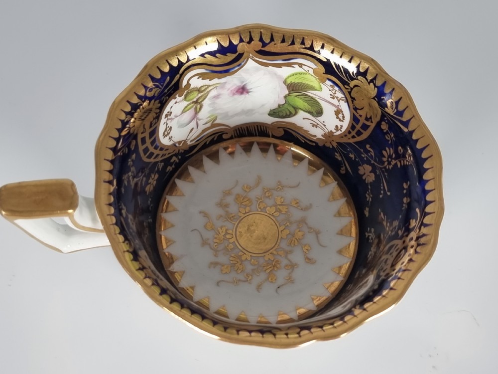 An early nineteenth-century Coalport porcelain cabinet trio featuring a teacup, coffee cup, and saucer styled with cobalt blue borders, gilded detailing, and hand-painted white rose panels. View XII