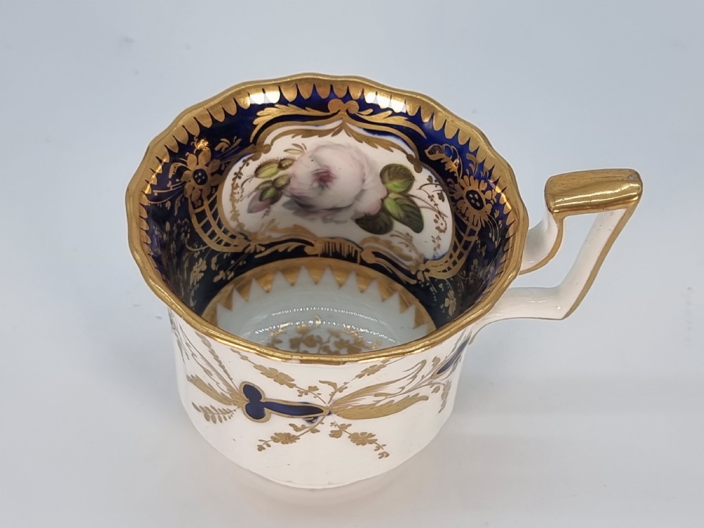 An early nineteenth-century Coalport porcelain cabinet trio featuring a teacup, coffee cup, and saucer styled with cobalt blue borders, gilded detailing, and hand-painted white rose panels. View XIV