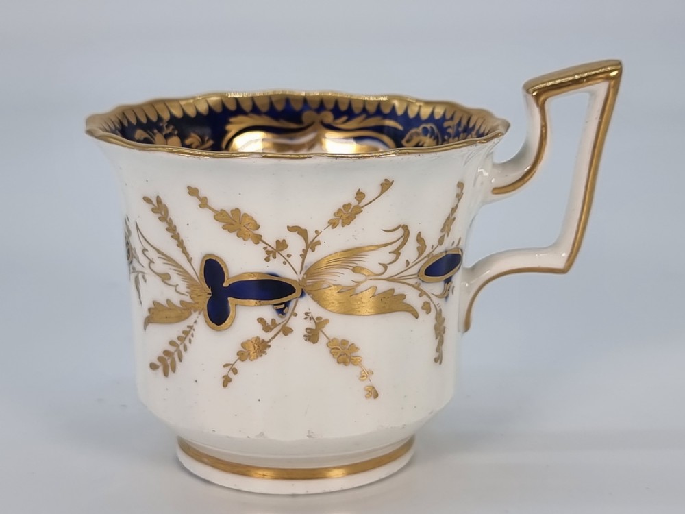 An early nineteenth-century Coalport porcelain cabinet trio featuring a teacup, coffee cup, and saucer styled with cobalt blue borders, gilded detailing, and hand-painted white rose panels. View XV