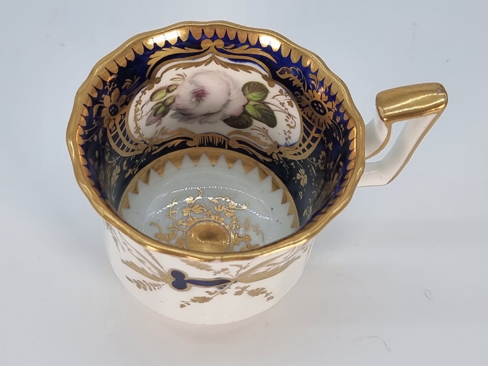 An early nineteenth-century Coalport porcelain cabinet trio featuring a teacup, coffee cup, and saucer styled with cobalt blue borders, gilded detailing, and hand-painted white rose panels. View XVII