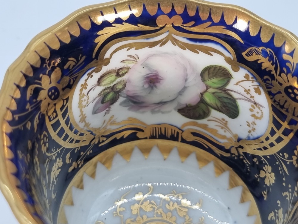 An early nineteenth-century Coalport porcelain cabinet trio featuring a teacup, coffee cup, and saucer styled with cobalt blue borders, gilded detailing, and hand-painted white rose panels. View XVIII