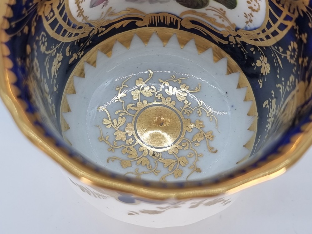 An early nineteenth-century Coalport porcelain cabinet trio featuring a teacup, coffee cup, and saucer styled with cobalt blue borders, gilded detailing, and hand-painted white rose panels. View XIX