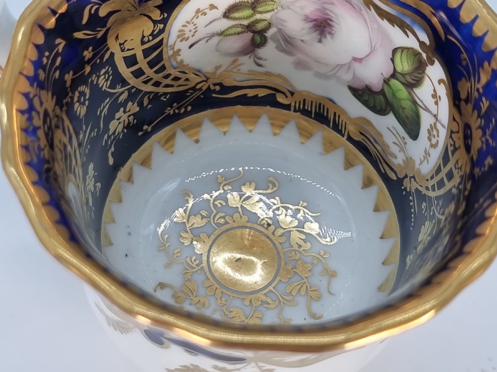 An early nineteenth-century Coalport porcelain cabinet trio featuring a teacup, coffee cup, and saucer styled with cobalt blue borders, gilded detailing, and hand-painted white rose panels. View XXI