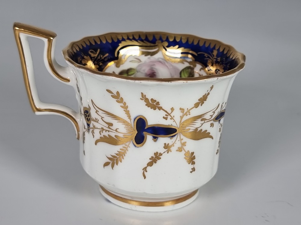 An early nineteenth-century Coalport porcelain cabinet trio featuring a teacup, coffee cup, and saucer styled with cobalt blue borders, gilded detailing, and hand-painted white rose panels. View XXII