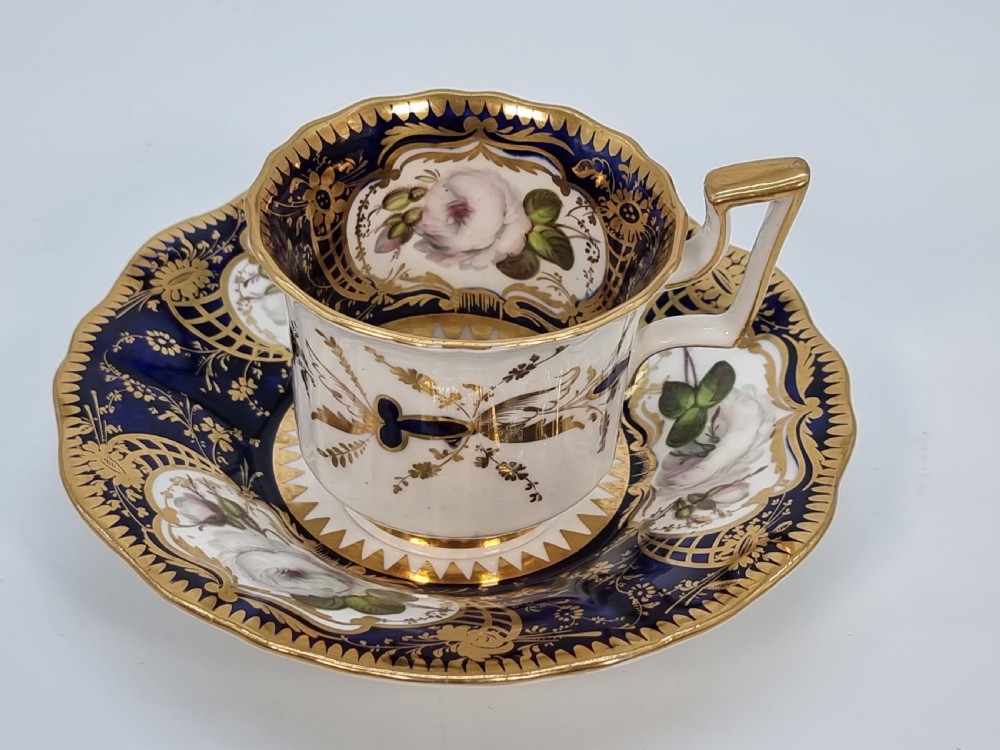 An early nineteenth-century Coalport porcelain cabinet trio featuring a teacup, coffee cup, and saucer styled with cobalt blue borders, gilded detailing, and hand-painted white rose panels. View XXIX