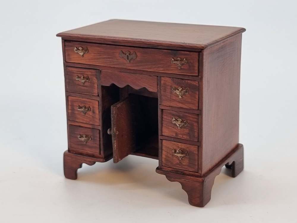 An antique miniature yew wood kneehole desk featuring small drawers, brass handles, and a central cupboard door. View XVII