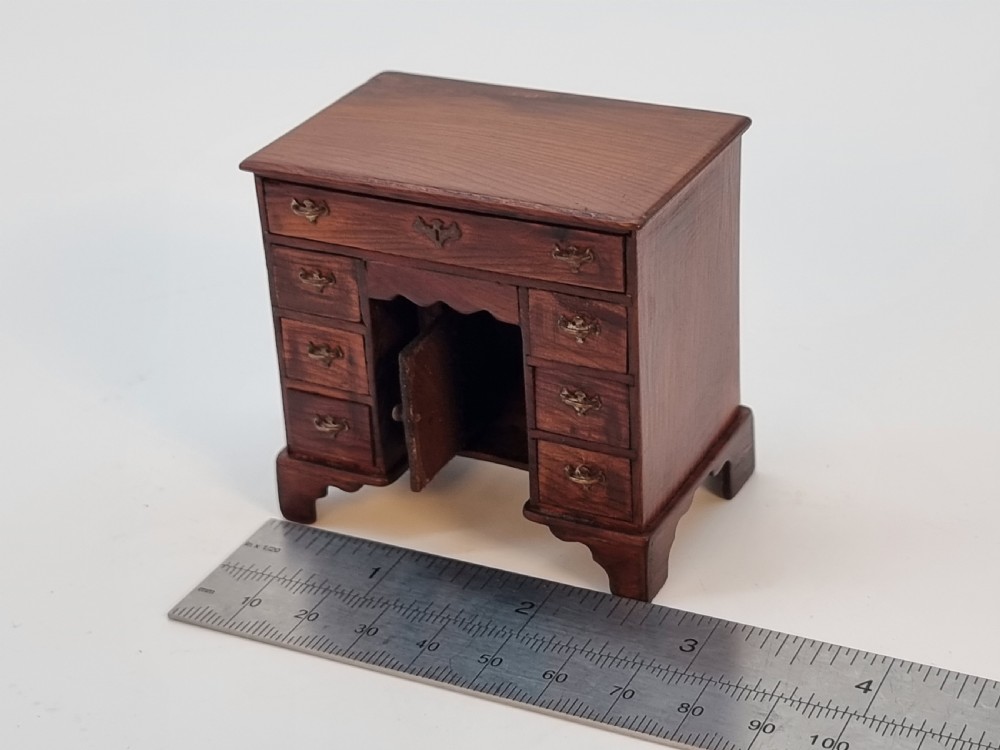 An antique miniature yew wood kneehole desk featuring small drawers, brass handles, and a central cupboard door. View XVIII