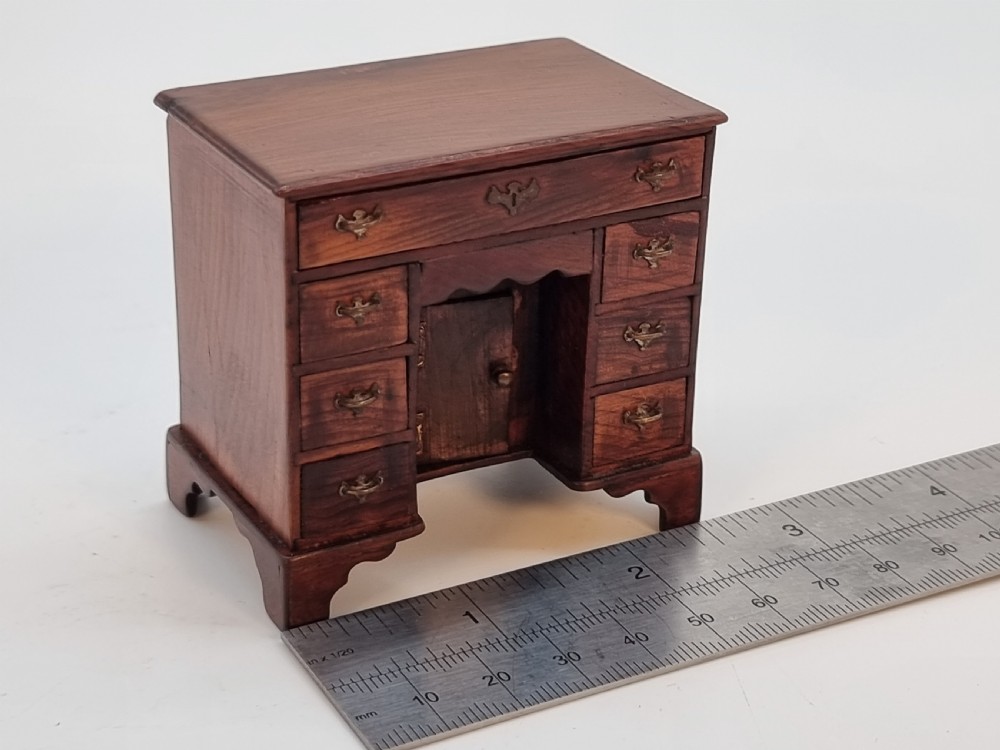 An antique miniature yew wood kneehole desk featuring small drawers, brass handles, and a central cupboard door. View XIX