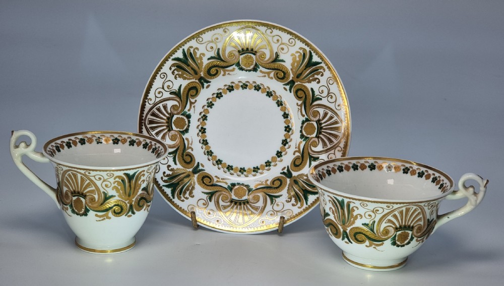 An early 19th-century Spode porcelain cabinet trio consisting of a teacup, coffee cup, and saucer adorned with intricate gold gilding and green scrollwork.