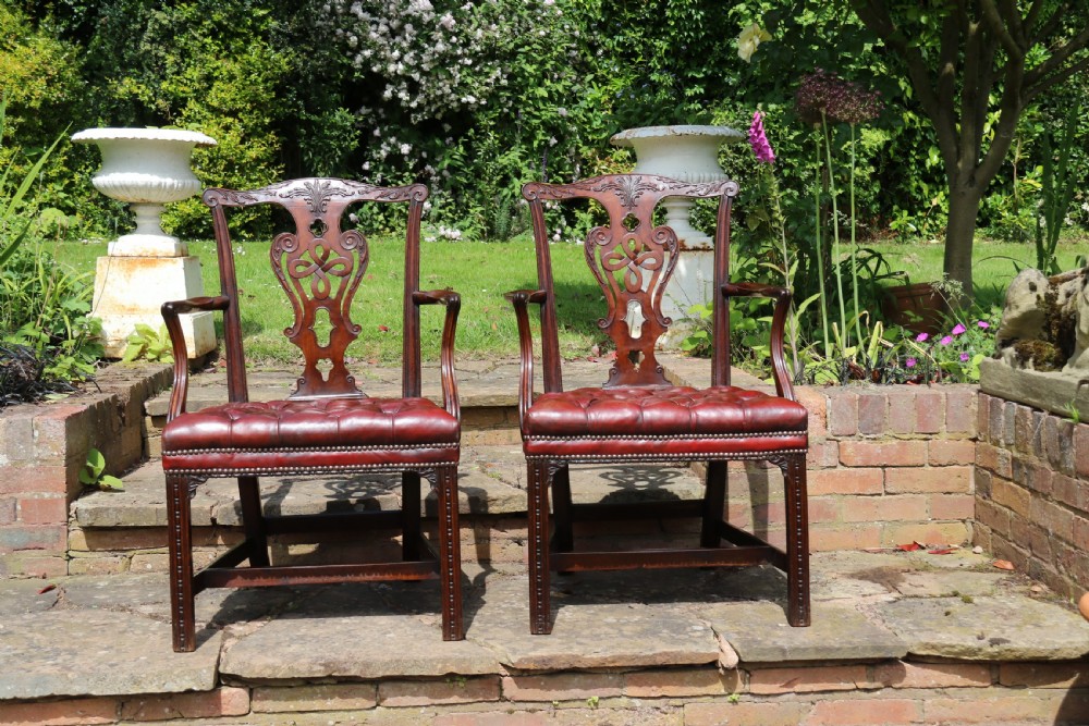 A pair of 18th-century George III Chippendale period mahogany armchairs featuring pierced carved back splats and deep red buttoned leather seats with brass stud trim. View IV