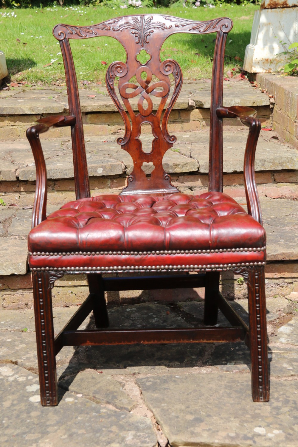 A pair of 18th-century George III Chippendale period mahogany armchairs featuring pierced carved back splats and deep red buttoned leather seats with brass stud trim. View X