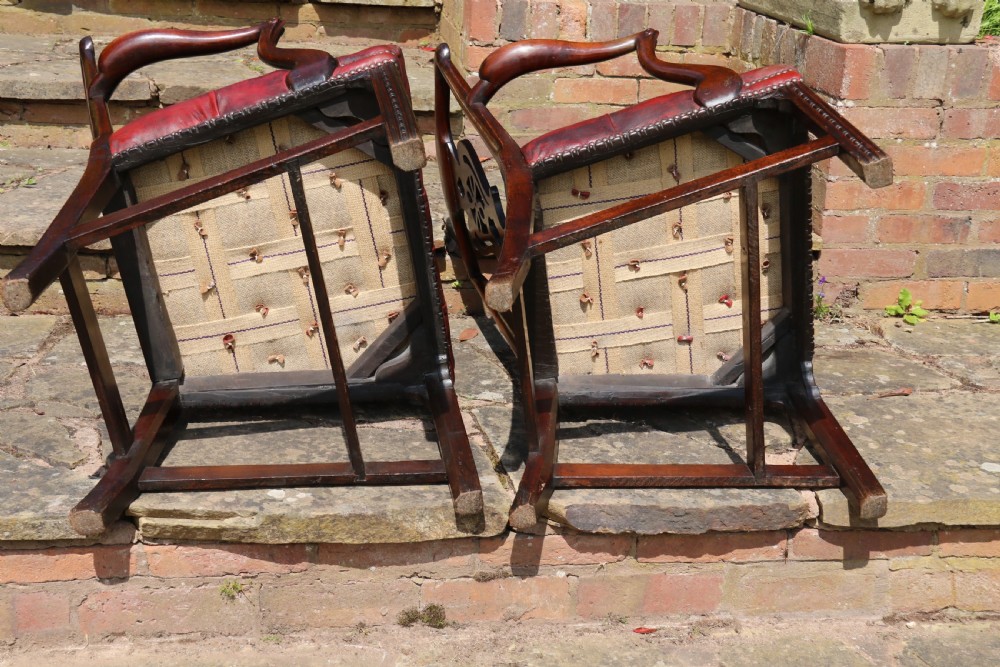 A pair of 18th-century George III Chippendale period mahogany armchairs featuring pierced carved back splats and deep red buttoned leather seats with brass stud trim. View XX