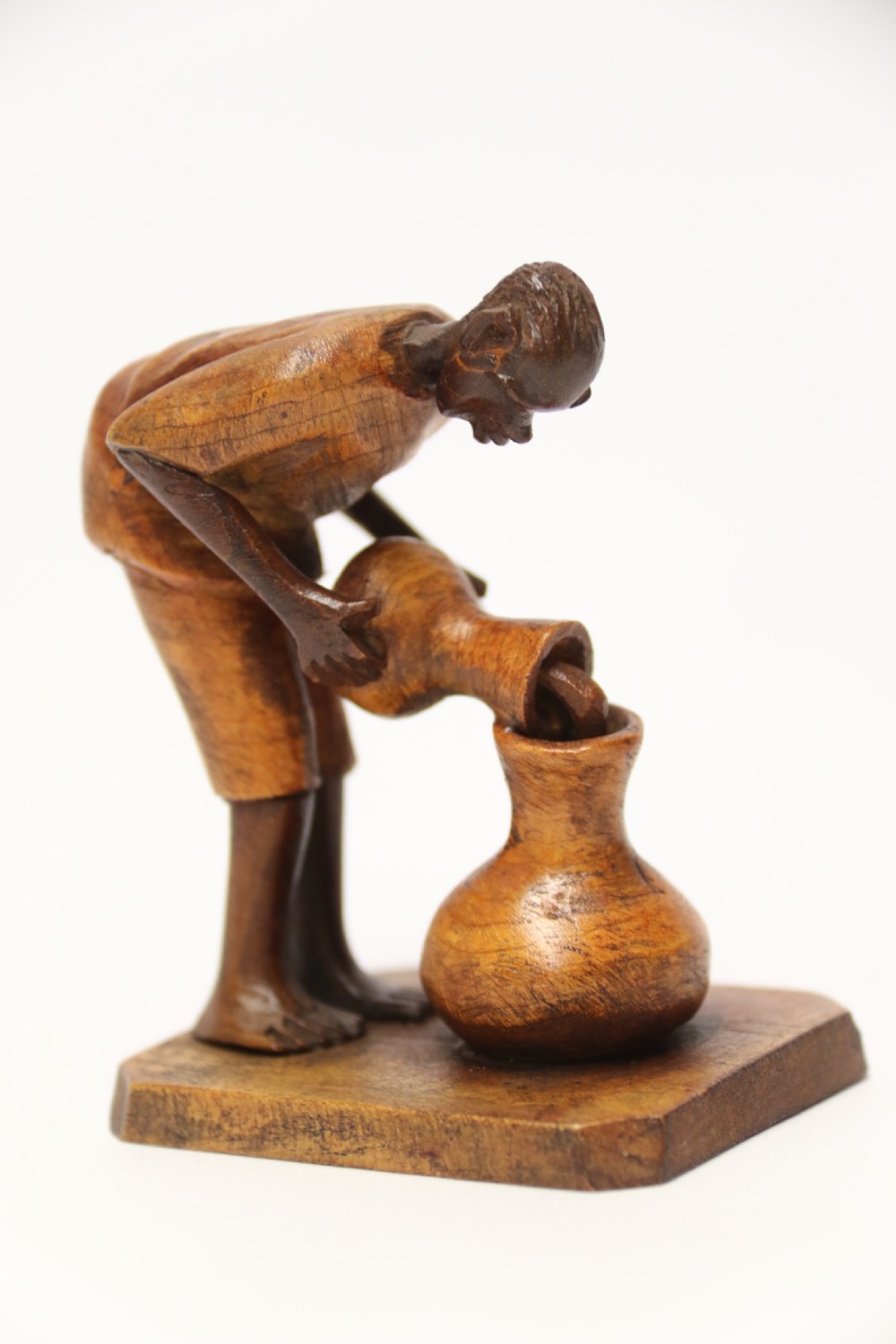 A collection of hand-carved warm brown hardwood figures from Nigeria depicting individuals engaged in daily tasks alongside a carved canoe. View II