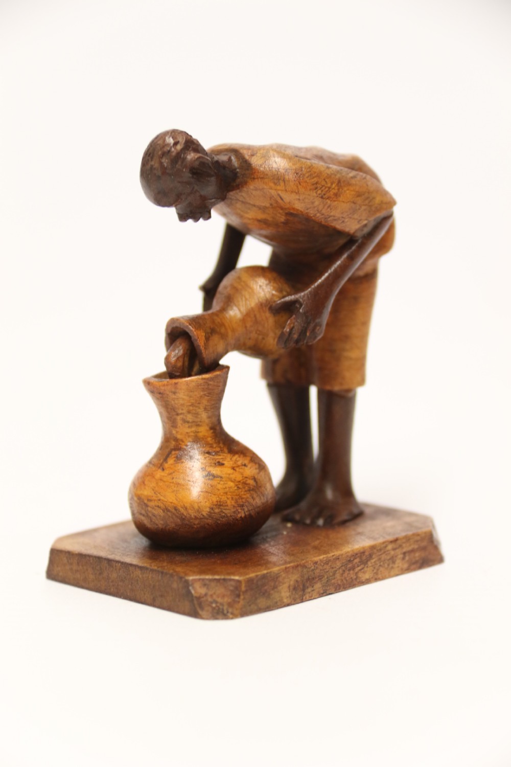 A collection of hand-carved warm brown hardwood figures from Nigeria depicting individuals engaged in daily tasks alongside a carved canoe. View III