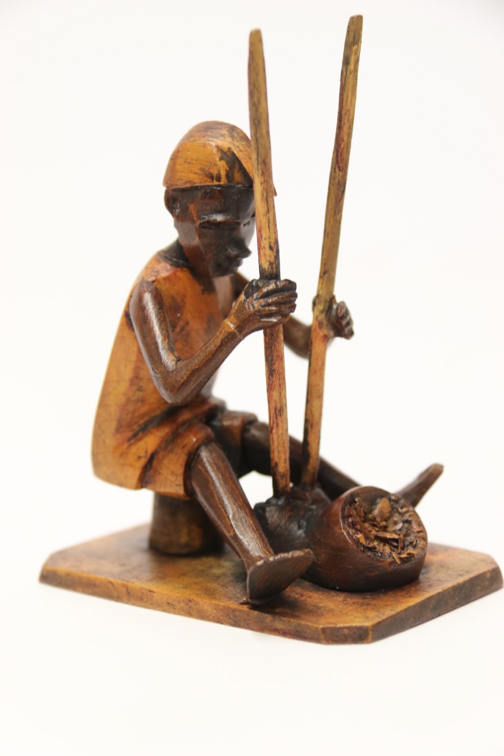 A collection of hand-carved warm brown hardwood figures from Nigeria depicting individuals engaged in daily tasks alongside a carved canoe. View V