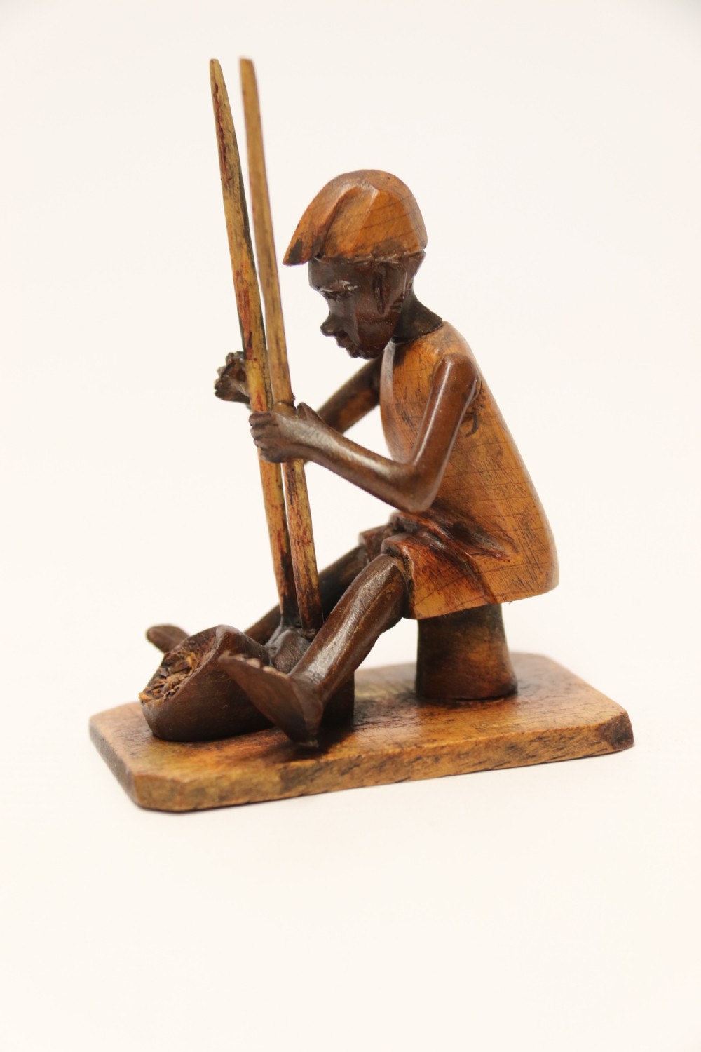A collection of hand-carved warm brown hardwood figures from Nigeria depicting individuals engaged in daily tasks alongside a carved canoe. View VI