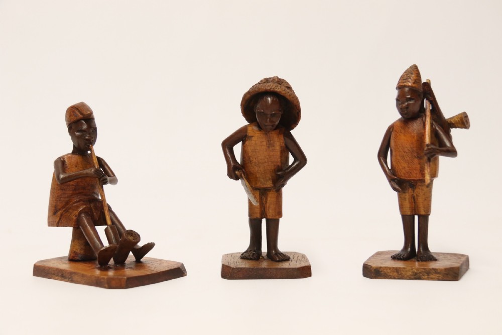 A collection of hand-carved warm brown hardwood figures from Nigeria depicting individuals engaged in daily tasks alongside a carved canoe. View VII