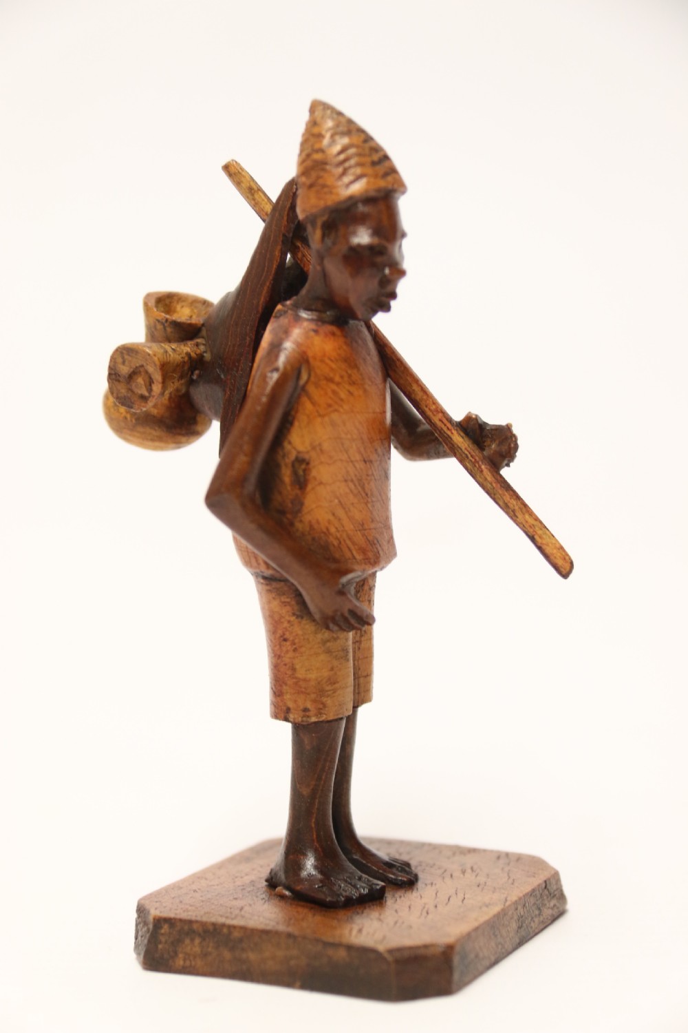 A collection of hand-carved warm brown hardwood figures from Nigeria depicting individuals engaged in daily tasks alongside a carved canoe. View XII