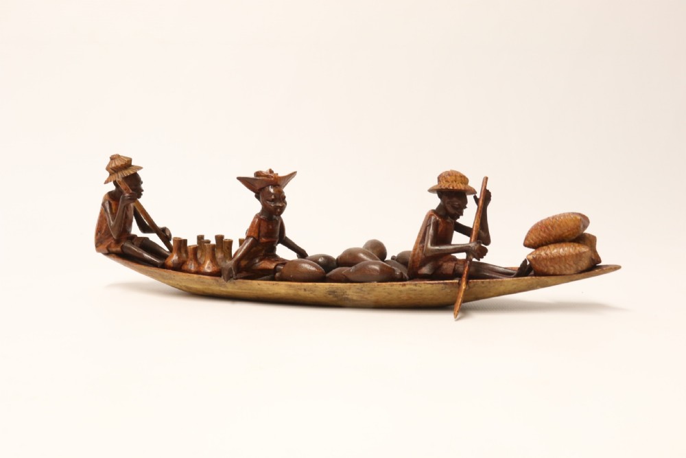 A collection of hand-carved warm brown hardwood figures from Nigeria depicting individuals engaged in daily tasks alongside a carved canoe. View XIV
