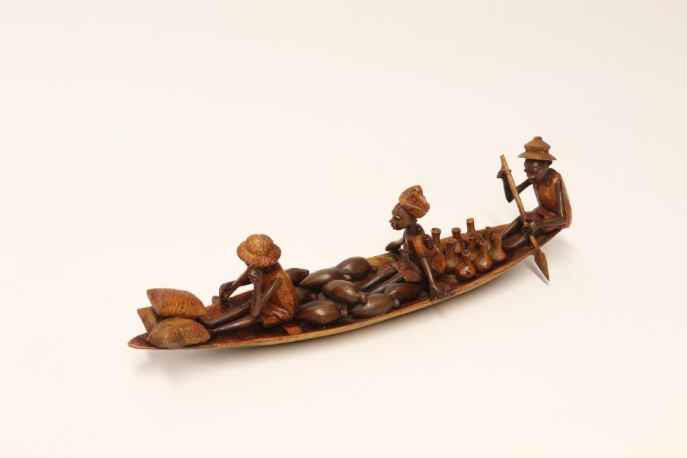 A collection of hand-carved warm brown hardwood figures from Nigeria depicting individuals engaged in daily tasks alongside a carved canoe. View XV