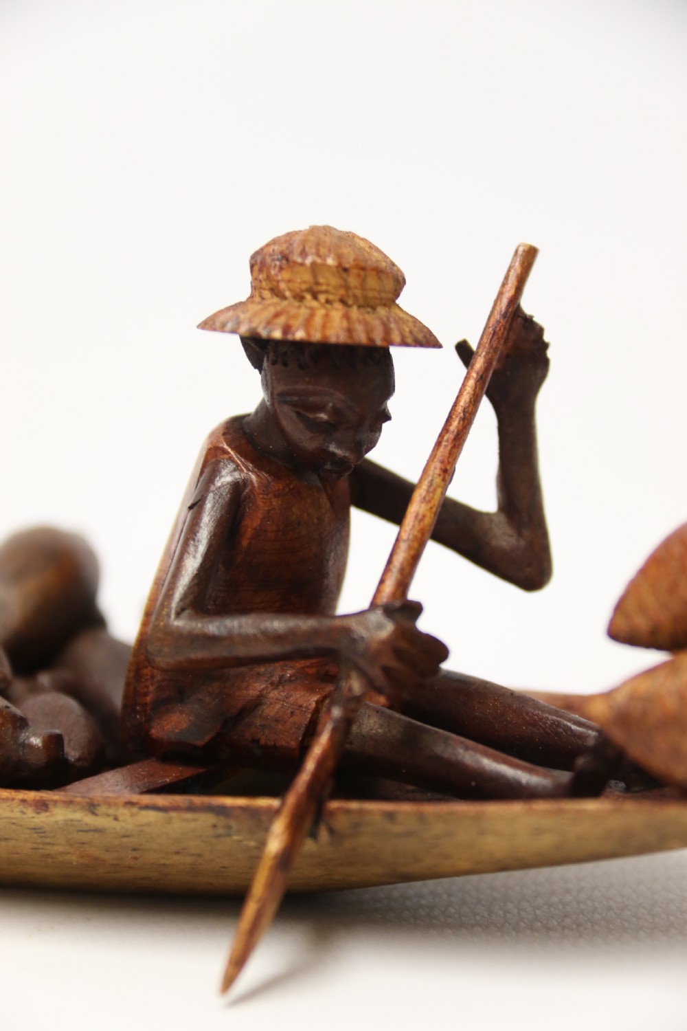 A collection of hand-carved warm brown hardwood figures from Nigeria depicting individuals engaged in daily tasks alongside a carved canoe. View XVI