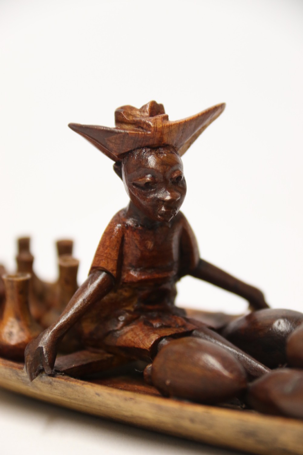 A collection of hand-carved warm brown hardwood figures from Nigeria depicting individuals engaged in daily tasks alongside a carved canoe. View XVII