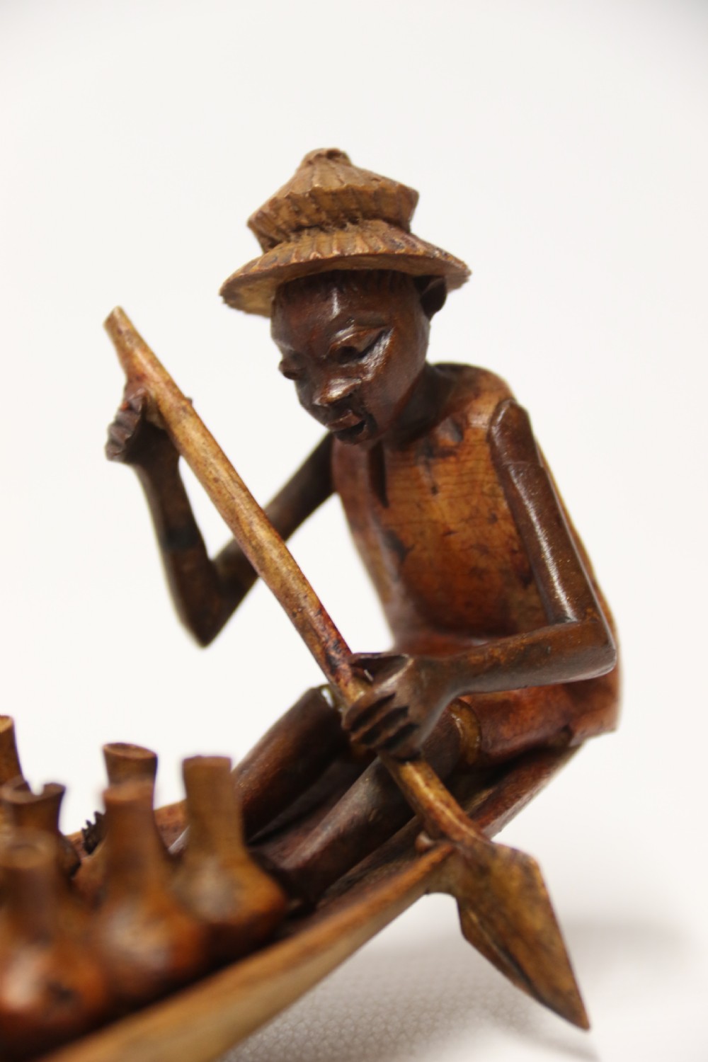 A collection of hand-carved warm brown hardwood figures from Nigeria depicting individuals engaged in daily tasks alongside a carved canoe. View XVIII