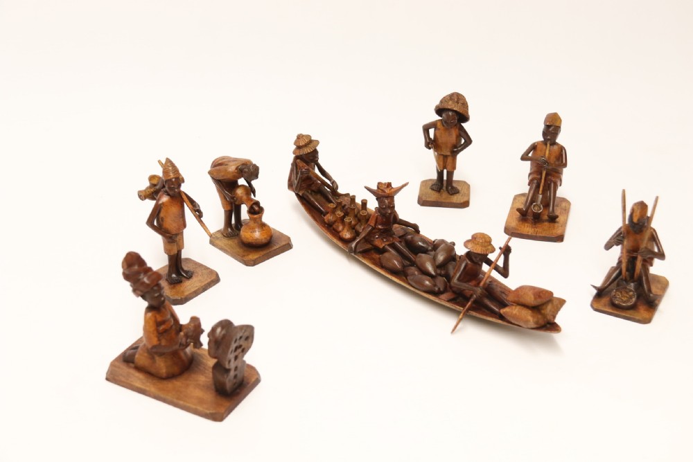A collection of hand-carved warm brown hardwood figures from Nigeria depicting individuals engaged in daily tasks alongside a carved canoe. View XIX