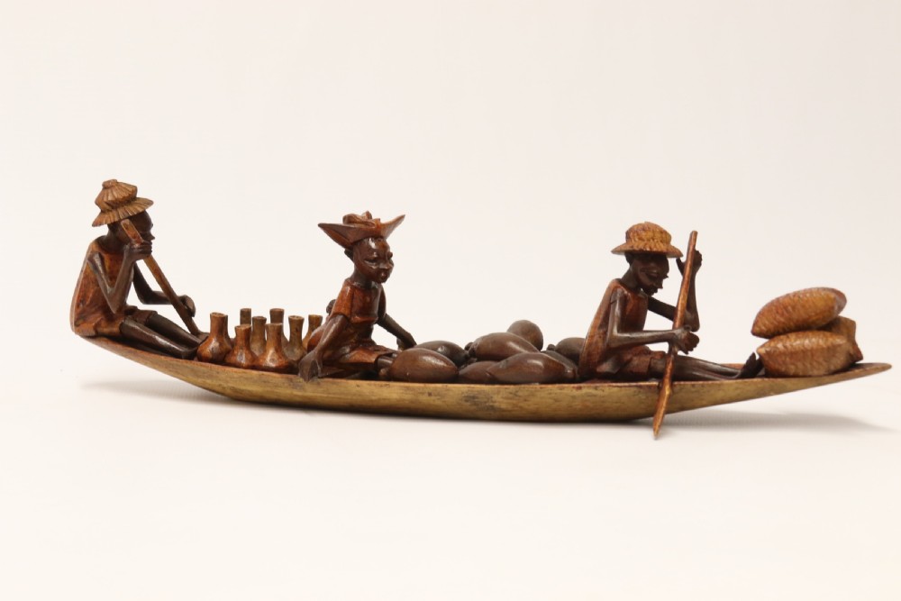 A collection of hand-carved warm brown hardwood figures from Nigeria depicting individuals engaged in daily tasks alongside a carved canoe. View XX