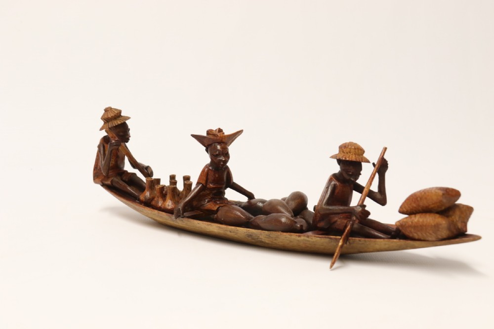 A collection of hand-carved warm brown hardwood figures from Nigeria depicting individuals engaged in daily tasks alongside a carved canoe. View XXI