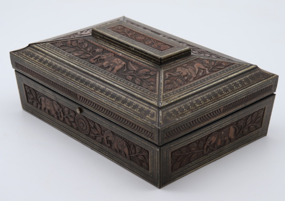 A rectangular lithographed tinplate box with a stepped lid, featuring embossed floral and elephant motifs designed to simulate carved wood.