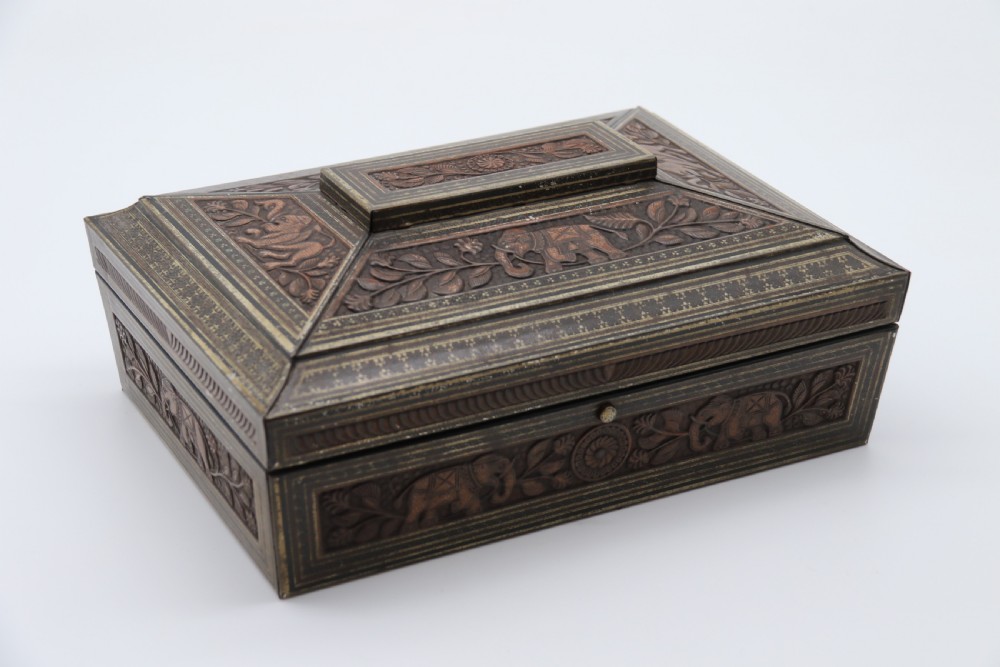 A rectangular lithographed tinplate box with a stepped lid, featuring embossed floral and elephant motifs designed to simulate carved wood. View II
