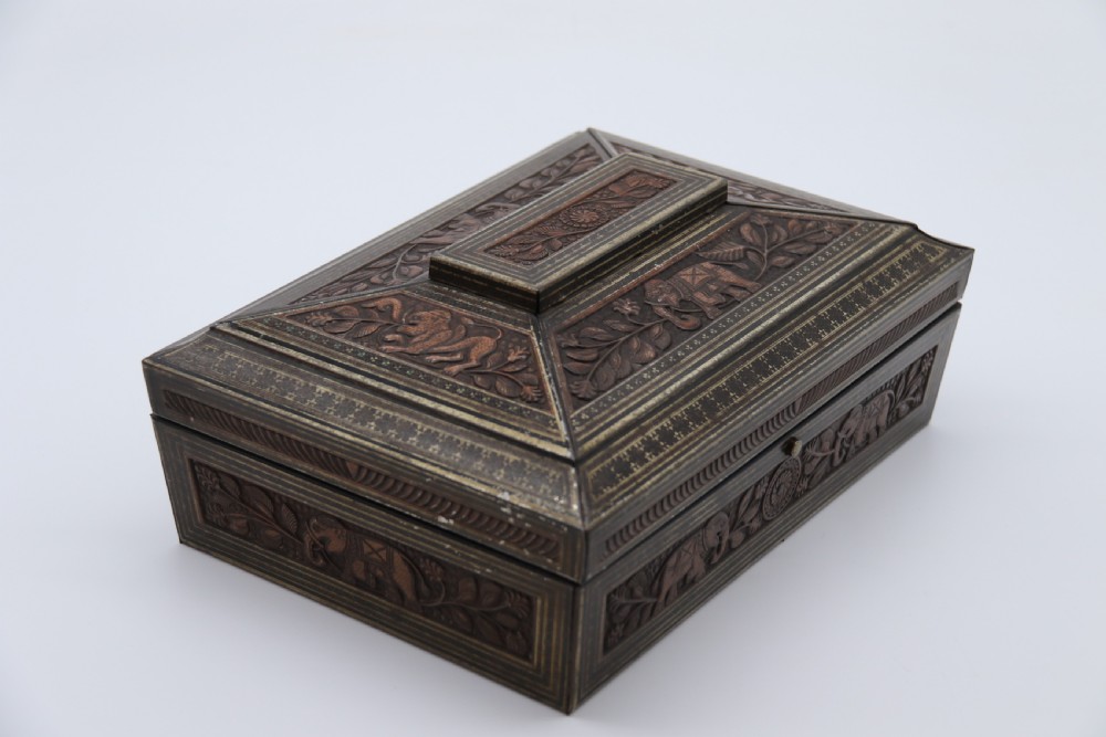 A rectangular lithographed tinplate box with a stepped lid, featuring embossed floral and elephant motifs designed to simulate carved wood. View III
