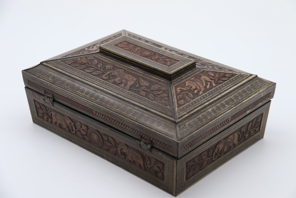 A rectangular lithographed tinplate box with a stepped lid, featuring embossed floral and elephant motifs designed to simulate carved wood. View V