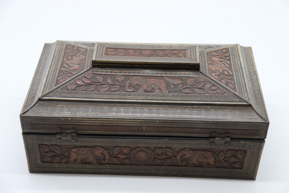 A rectangular lithographed tinplate box with a stepped lid, featuring embossed floral and elephant motifs designed to simulate carved wood. View VI