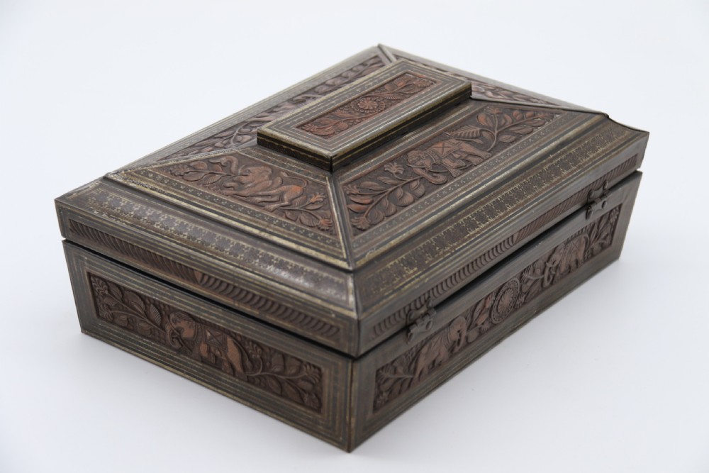A rectangular lithographed tinplate box with a stepped lid, featuring embossed floral and elephant motifs designed to simulate carved wood. View VII