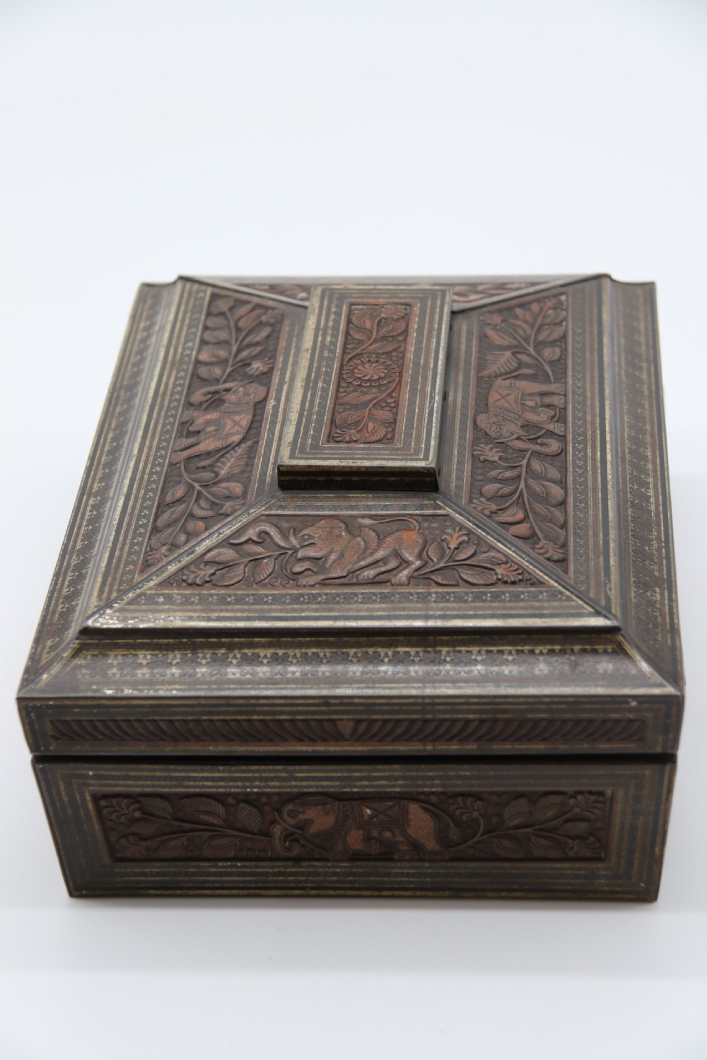 A rectangular lithographed tinplate box with a stepped lid, featuring embossed floral and elephant motifs designed to simulate carved wood. View VIII