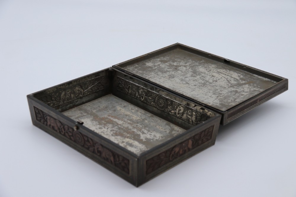 A rectangular lithographed tinplate box with a stepped lid, featuring embossed floral and elephant motifs designed to simulate carved wood. View XI