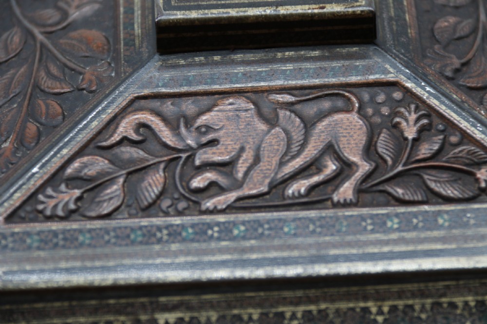 A rectangular lithographed tinplate box with a stepped lid, featuring embossed floral and elephant motifs designed to simulate carved wood. View XV