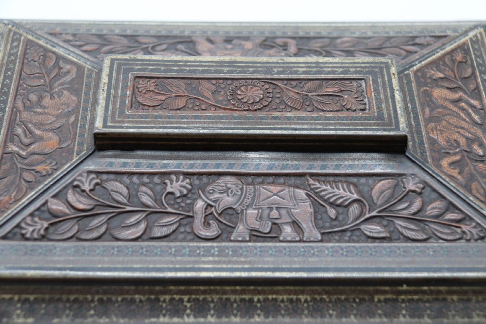 A rectangular lithographed tinplate box with a stepped lid, featuring embossed floral and elephant motifs designed to simulate carved wood. View XVI