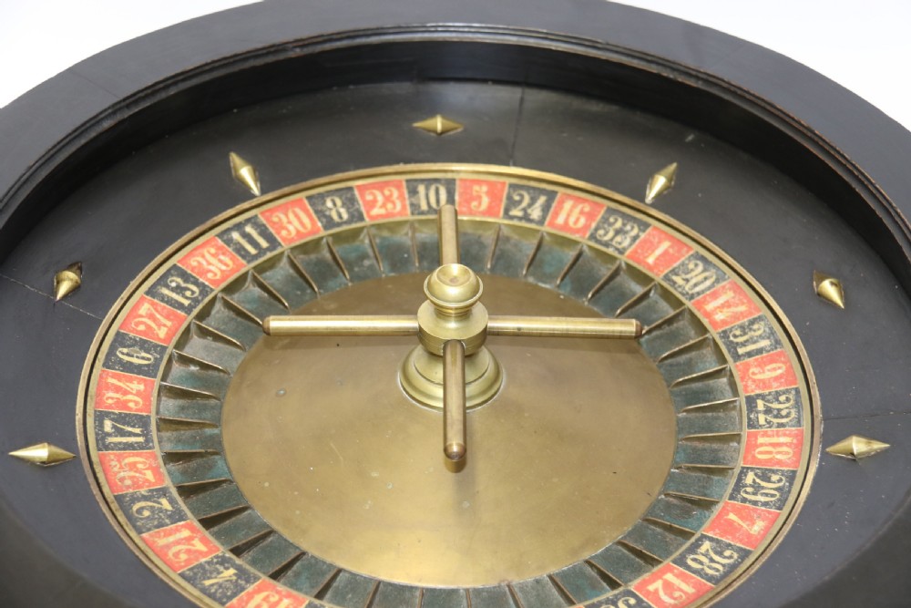 An antique French roulette wheel with ebonised wood casing and brass claw feet, set in front of an original dark green felt layout cloth printed with gold French gaming text. View II