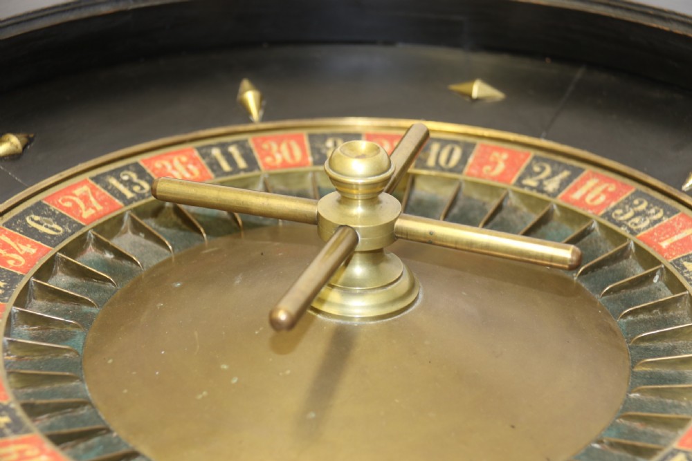 An antique French roulette wheel with ebonised wood casing and brass claw feet, set in front of an original dark green felt layout cloth printed with gold French gaming text. View XIII